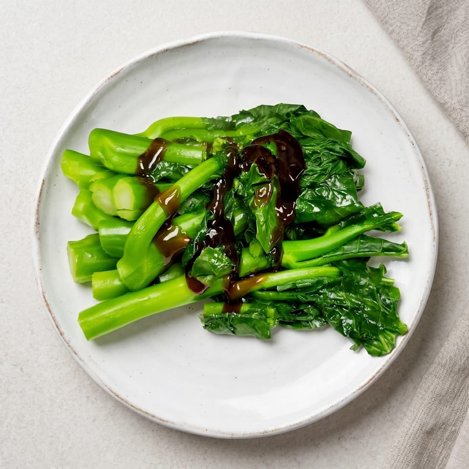 Steamed green Chinese broccoli (Gai Lan) with oyster sauce on a white plate.