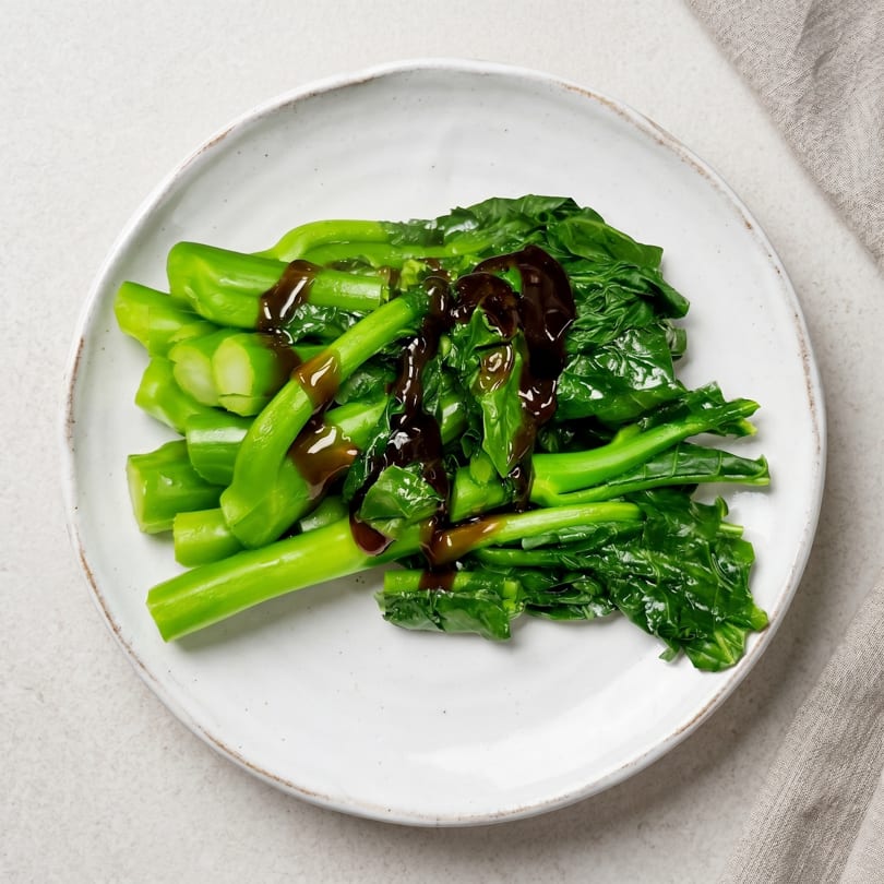 Steamed green Chinese broccoli (Gai Lan) with oyster sauce on a white plate.